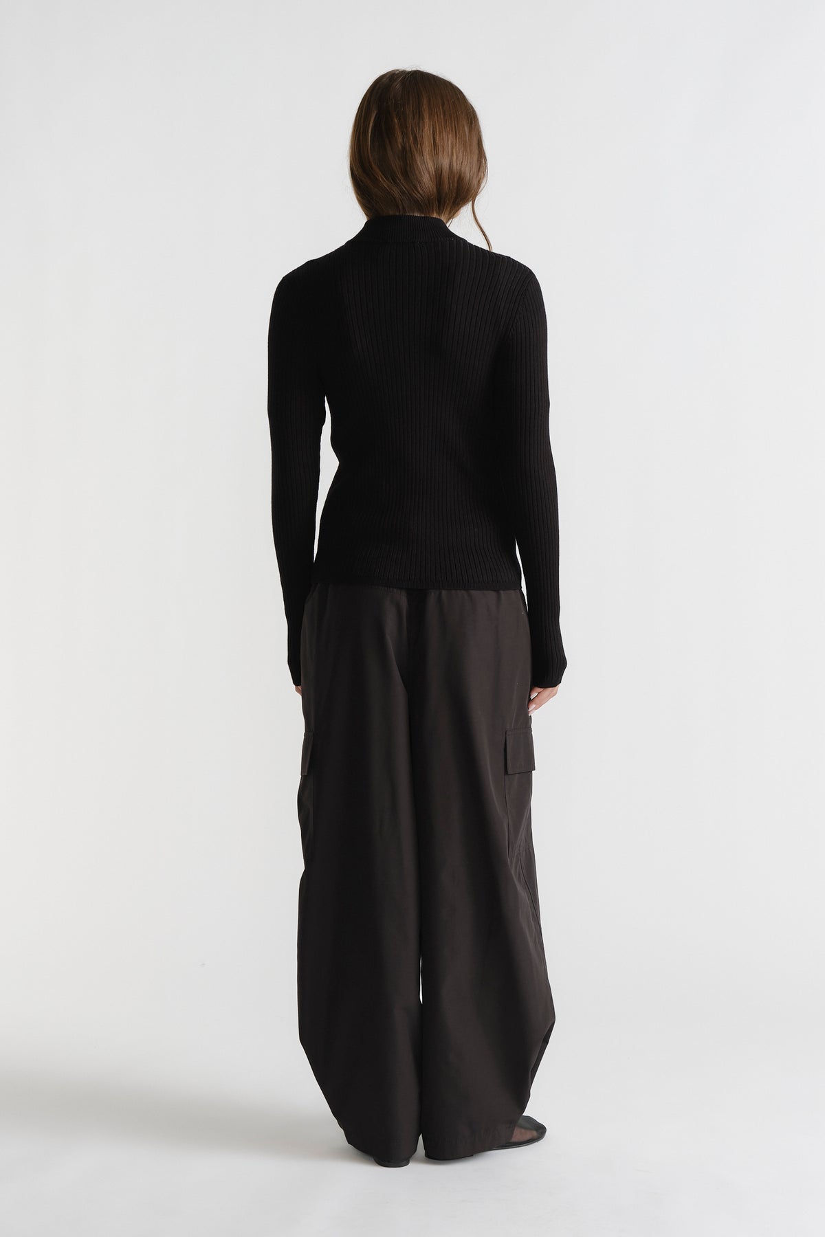 Back view of D-Luxe Knit Zip Long Sleeve in black with ribbed texture paired with wide-leg dark pants by DECJUBA.