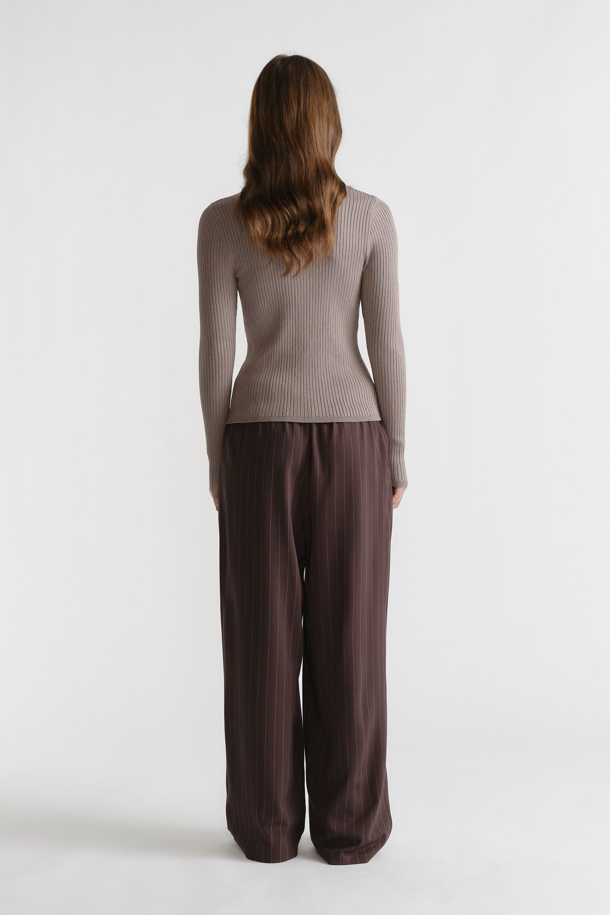 Woman wearing a dune-toned D-Luxe Knit Zip Long Sleeve with ribbed texture, paired with loose-fitting brown pants for a relaxed look