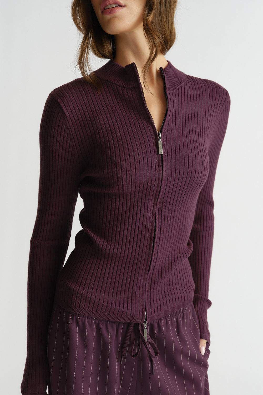 Close-up of a woman wearing a plum ribbed knit zip-up long sleeve top with matching striped pants and side pockets.