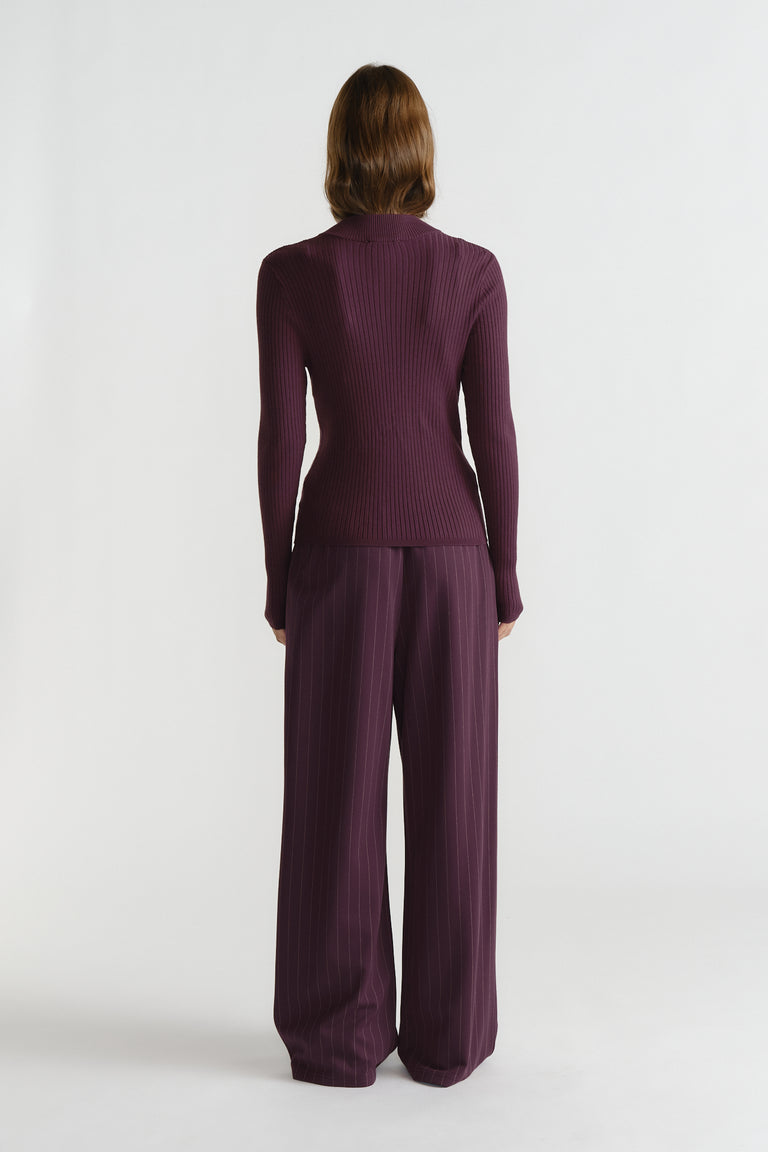 Back view of woman wearing a ribbed, long sleeve knit top paired with wide-leg pinstriped trousers in deep purple.