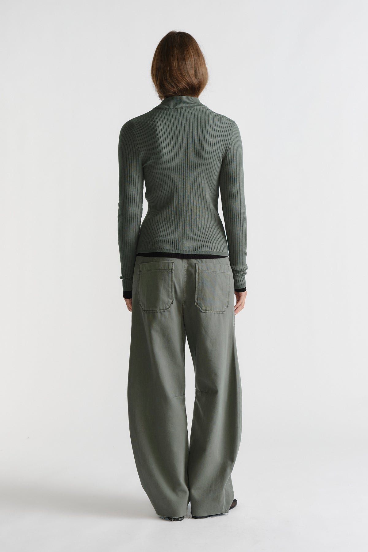 Woman wearing D-Luxe Knit Zip Long Sleeve in muted green, styled with relaxed wide-leg pants for a casual look by DECJUBA