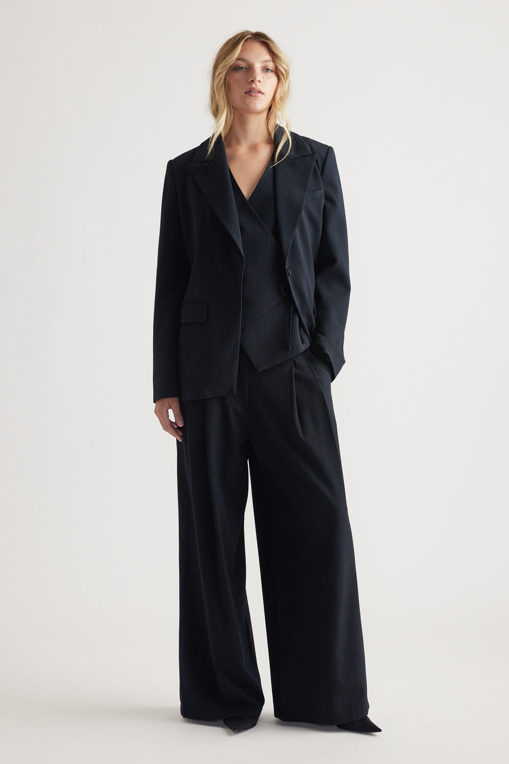 Woman dressed in tailored black pinstripe blazer and matching wide-leg pleated pants for a polished look