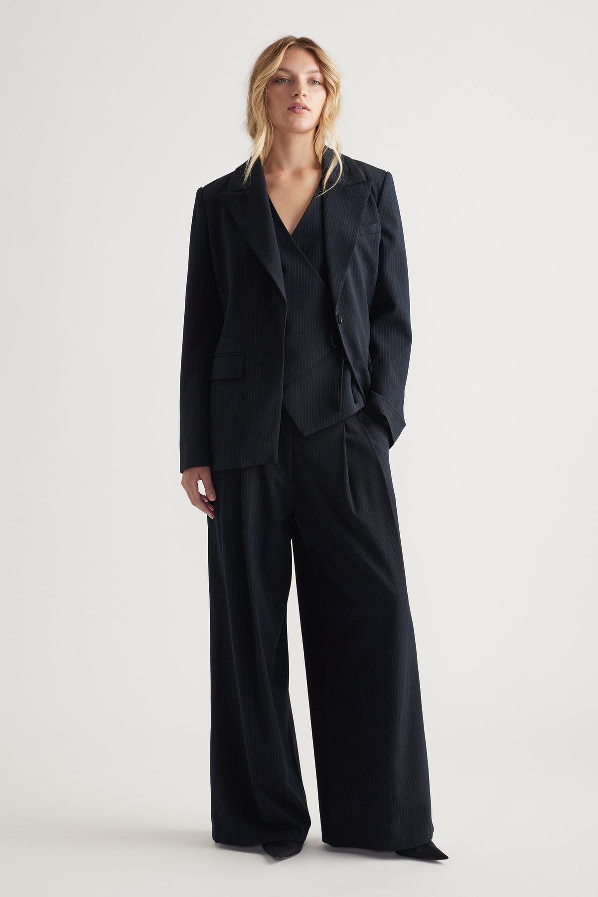 Woman dressed in tailored black pinstripe blazer and matching wide-leg pleated pants for a polished look