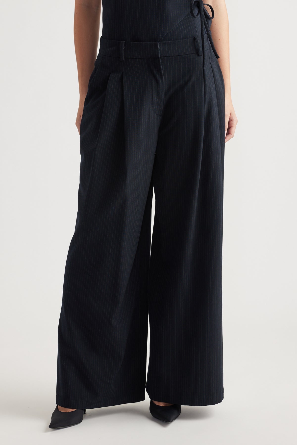 Navy wide-leg pleated pants with subtle pinstripe, featuring belt loops and deep side pockets for a polished look.