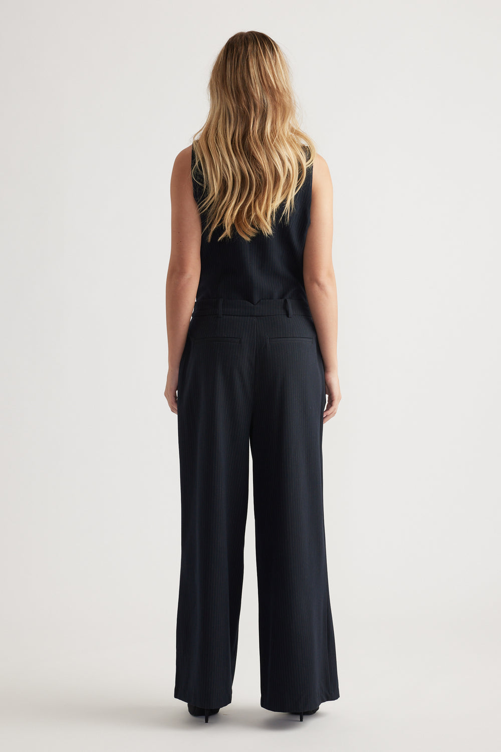 Back view of navy pleated wide-leg pants styled with a sleeveless ribbed top against a plain background