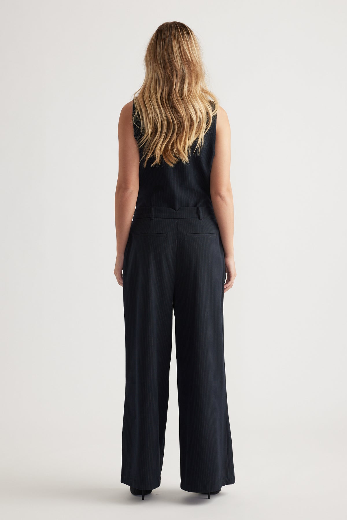 Back view of navy pleated wide-leg pants styled with a sleeveless ribbed top against a plain background