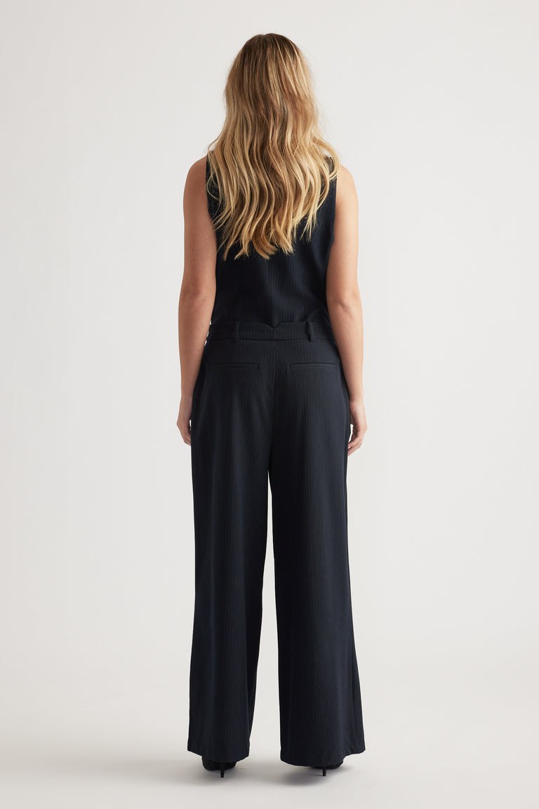 Back view of navy pleated wide-leg pants styled with a sleeveless ribbed top against a plain background