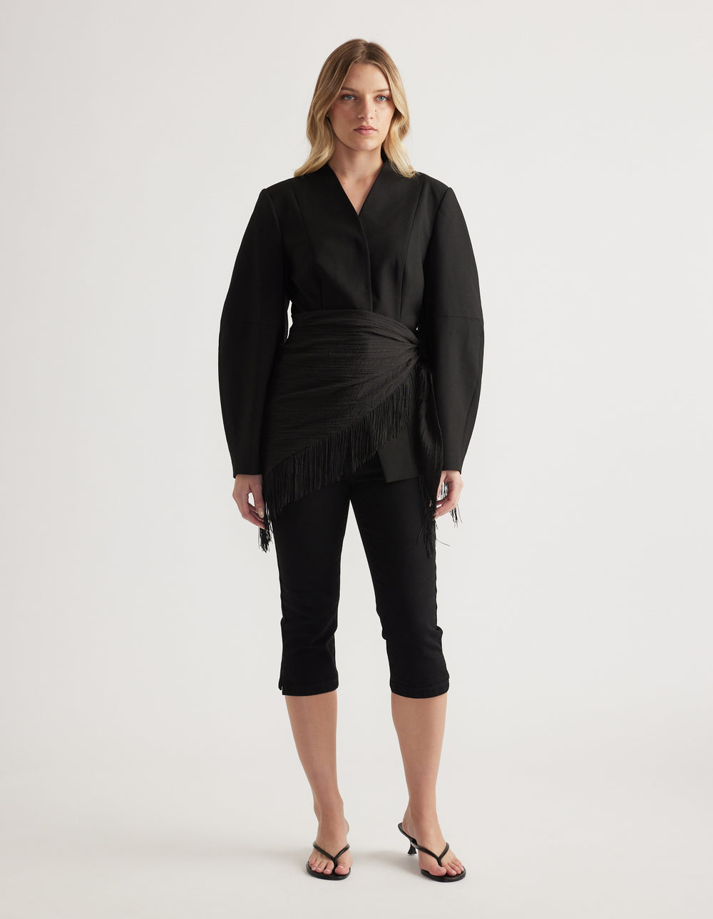 Woman wearing a tailored black blazer with long barrel sleeves styled with cropped black pants and heeled sandals