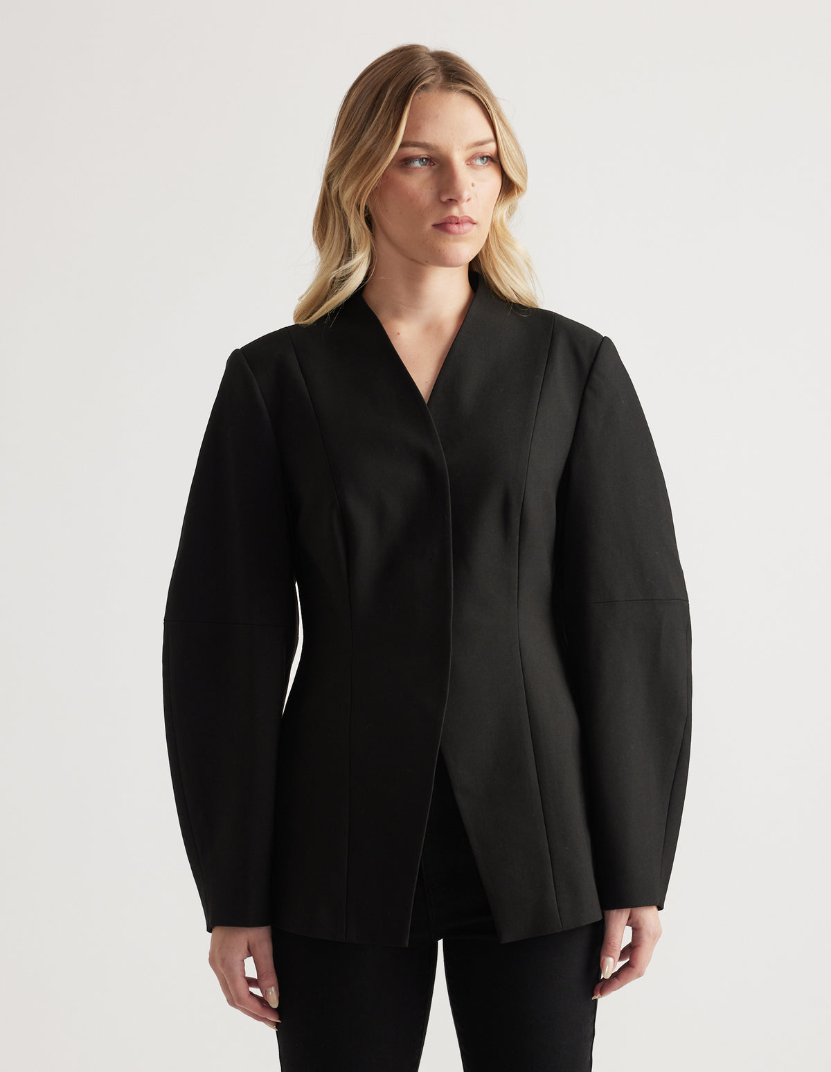Woman wearing a tailored black blazer with long barrel sleeves and a subtle textured finish, styled with black pants