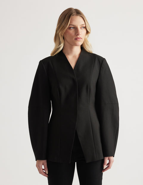 Woman wearing a tailored black blazer with long barrel sleeves and a subtle textured finish, styled with black pants
