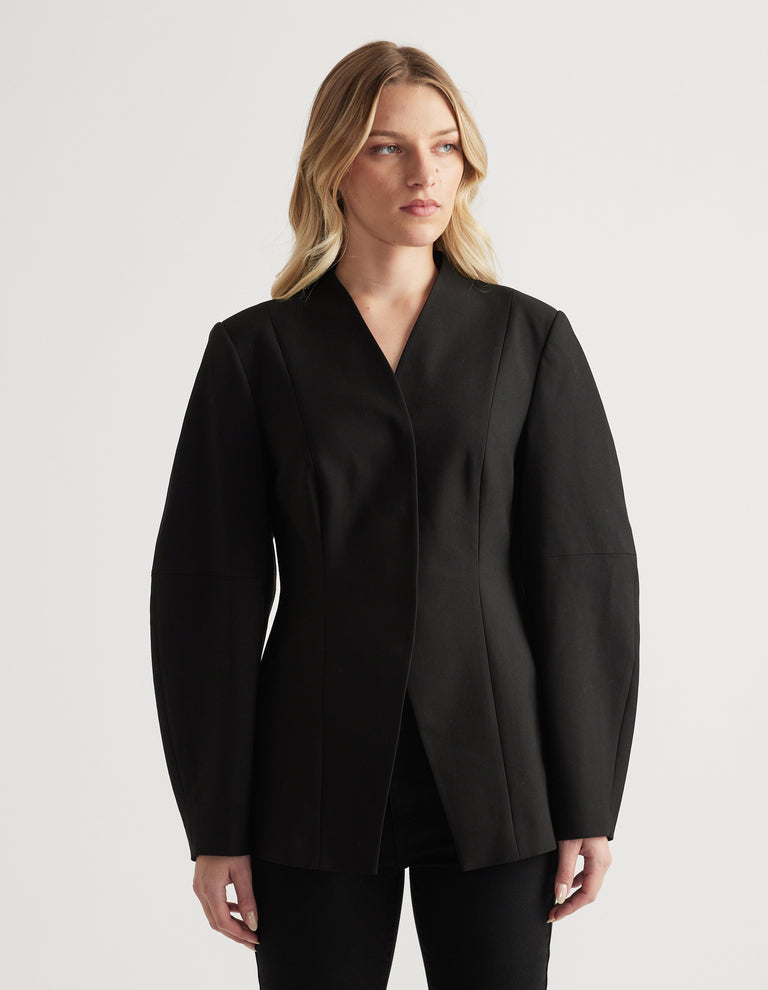 Woman wearing a tailored black blazer with long barrel sleeves and a subtle textured finish, styled with black pants