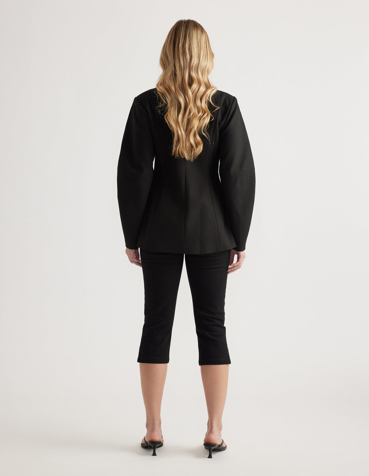 Woman shown from behind wearing a tailored black blazer with long barrel sleeves paired with cropped black pants