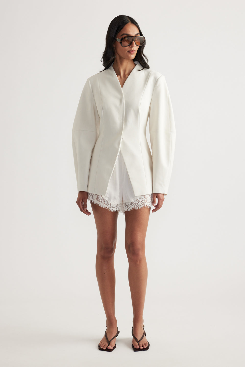 Model in an ivory blazer with long sleeves, lace-trim shorts, sunglasses and black strappy heels