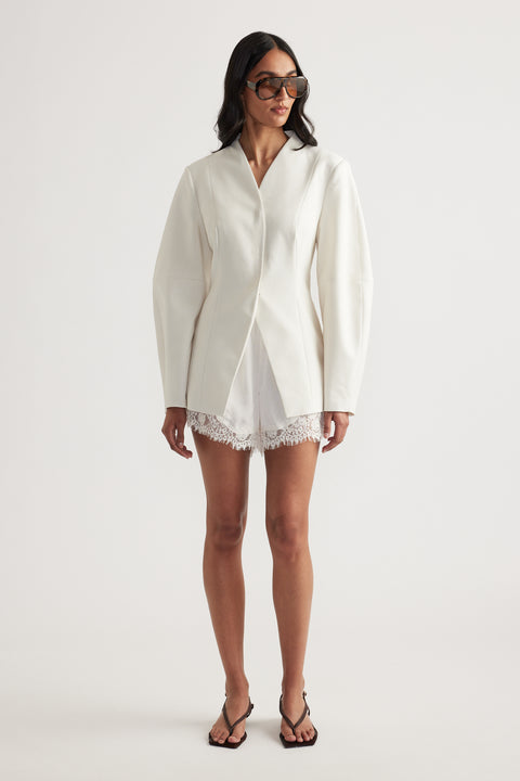Model in an ivory blazer with long sleeves, lace-trim shorts, sunglasses and black strappy heels