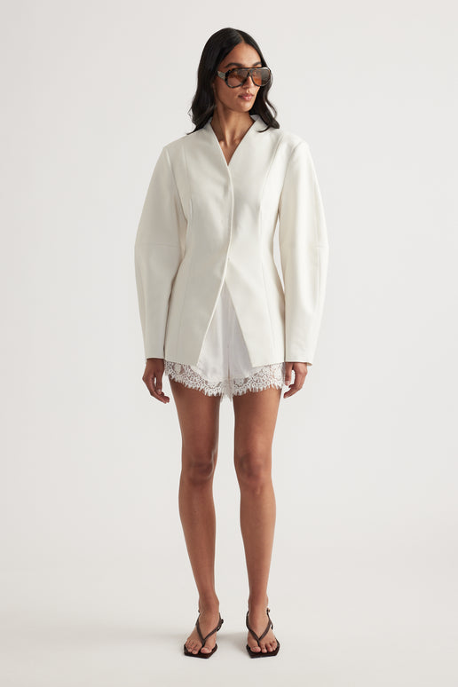 Model in an ivory blazer with long sleeves, lace-trim shorts, sunglasses and black strappy heels