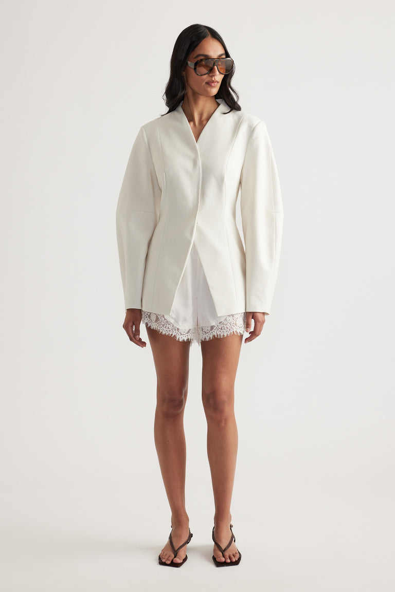 Model in an ivory blazer with long sleeves, lace-trim shorts, sunglasses and black strappy heels