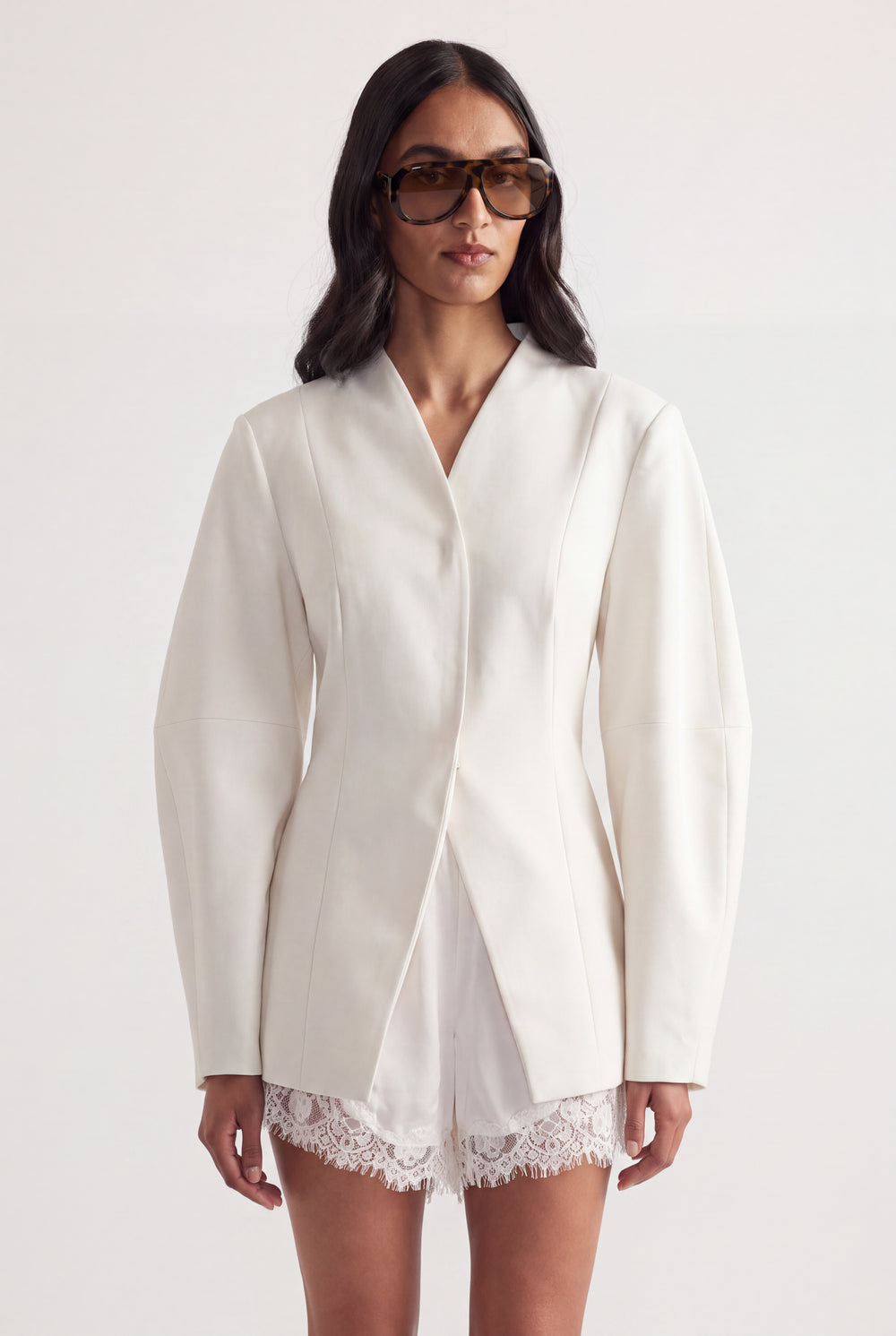 Woman in an ivory tailored blazer with long sleeves layered over white lace shorts