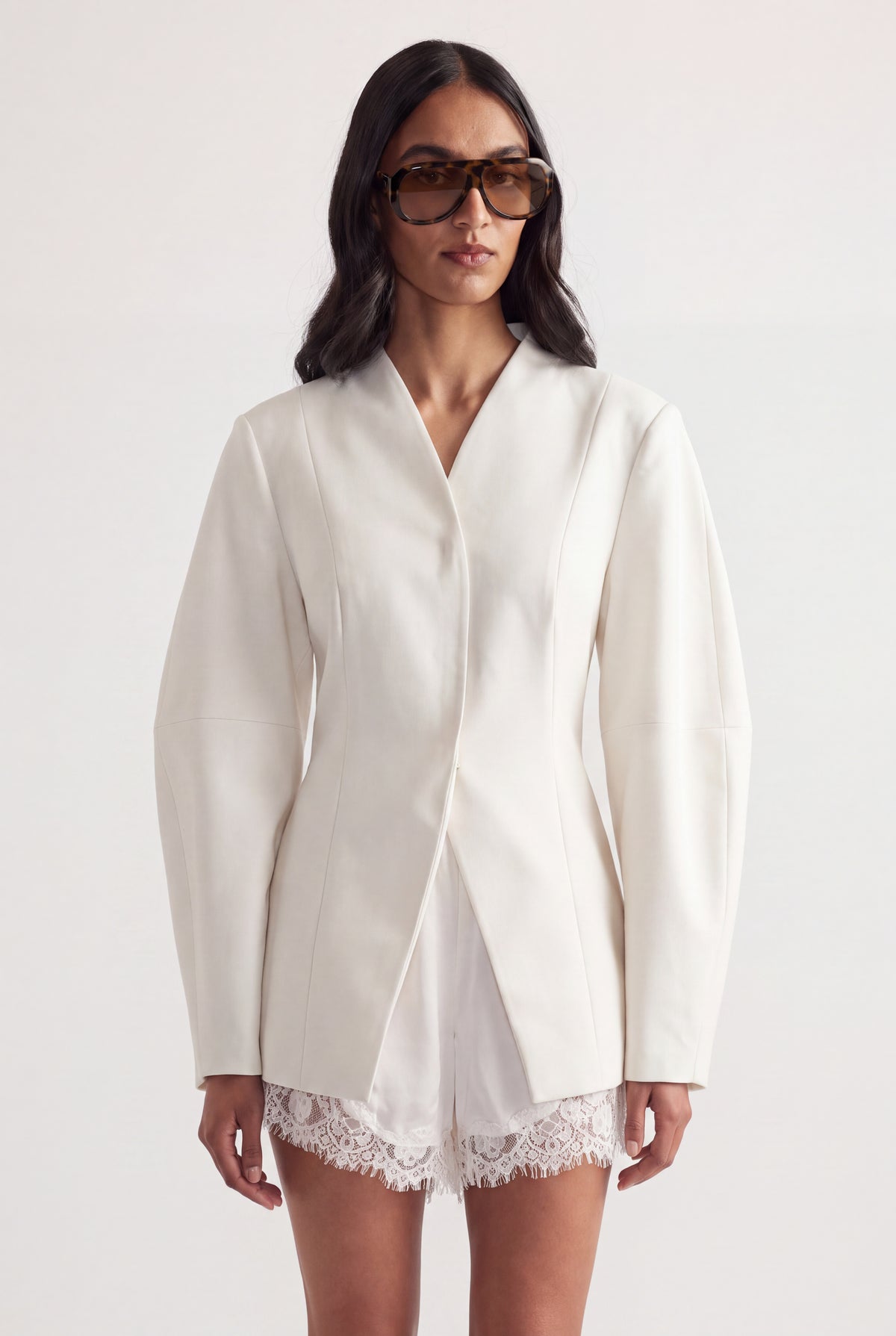 Woman in an ivory tailored blazer with long sleeves layered over white lace shorts
