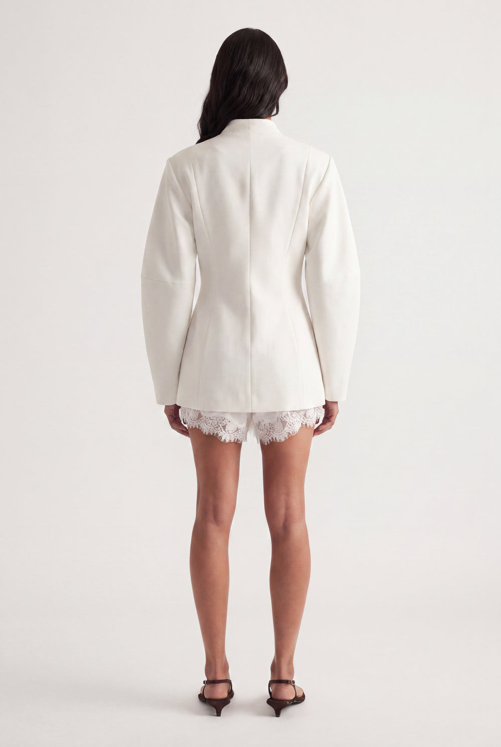 Back view of woman wearing an ivory tailored blazer over white lace shorts with black heels