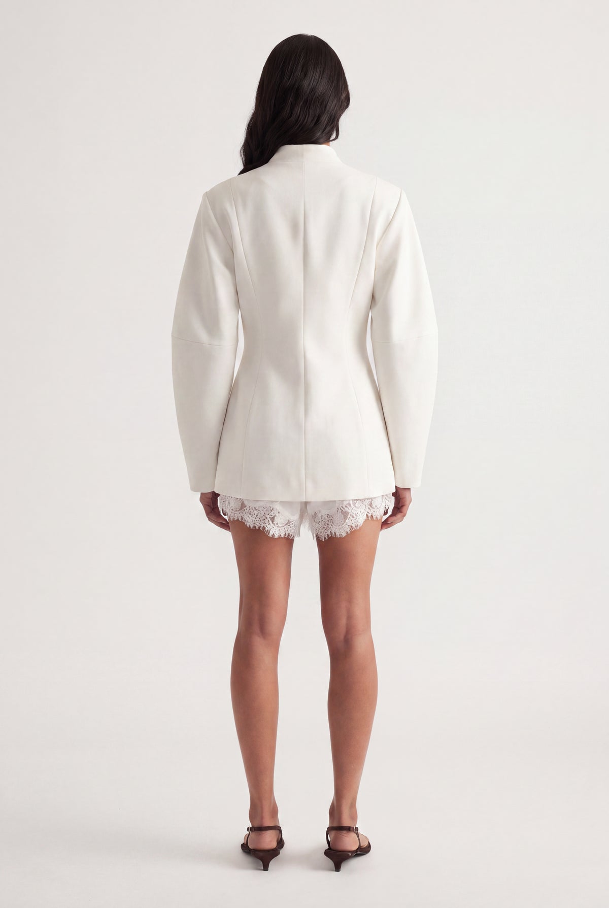 Back view of woman wearing an ivory tailored blazer over white lace shorts with black heels