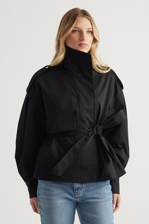 Woman wearing a belted black cropped trench coat with structured shoulders and high collar paired with blue jeans