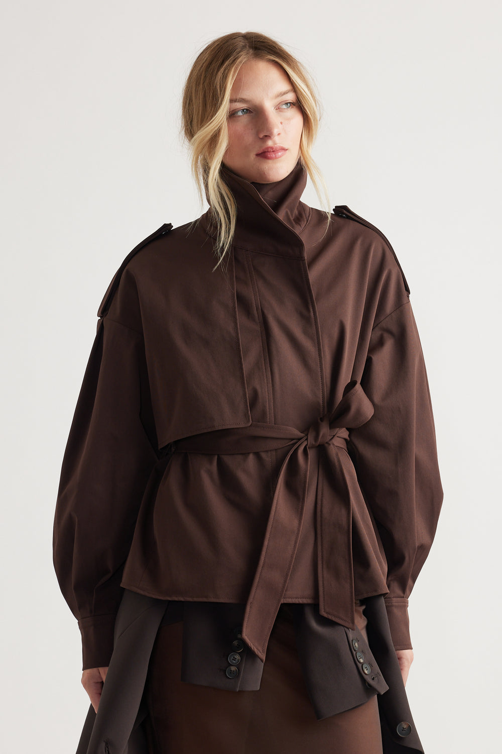 Woman wearing a dark chocolate cropped trench with a high collar and tied waist belt for a polished layered look