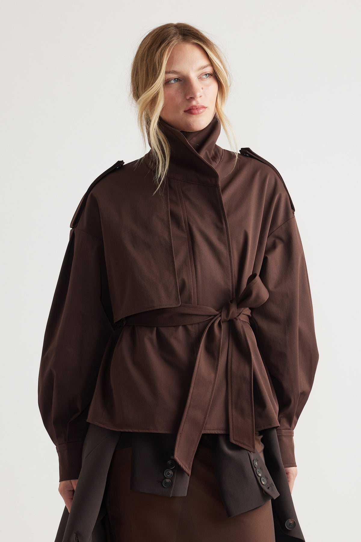 Woman wearing a dark chocolate cropped trench with a high collar and tied waist belt for a polished layered look