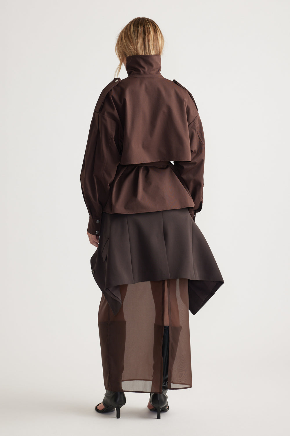 Woman seen from behind wearing a layered dark brown cropped trench with a high collar and sheer long skirt for an elegant look