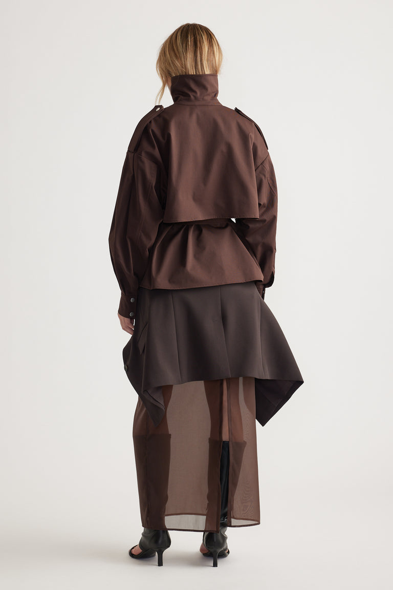 Woman seen from behind wearing a layered dark brown cropped trench with a high collar and sheer long skirt for an elegant look