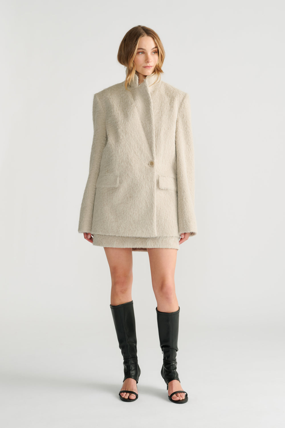 Model wearing a soft cream oversized blazer with long sleeves and notch lapels paired with black open-toe boots