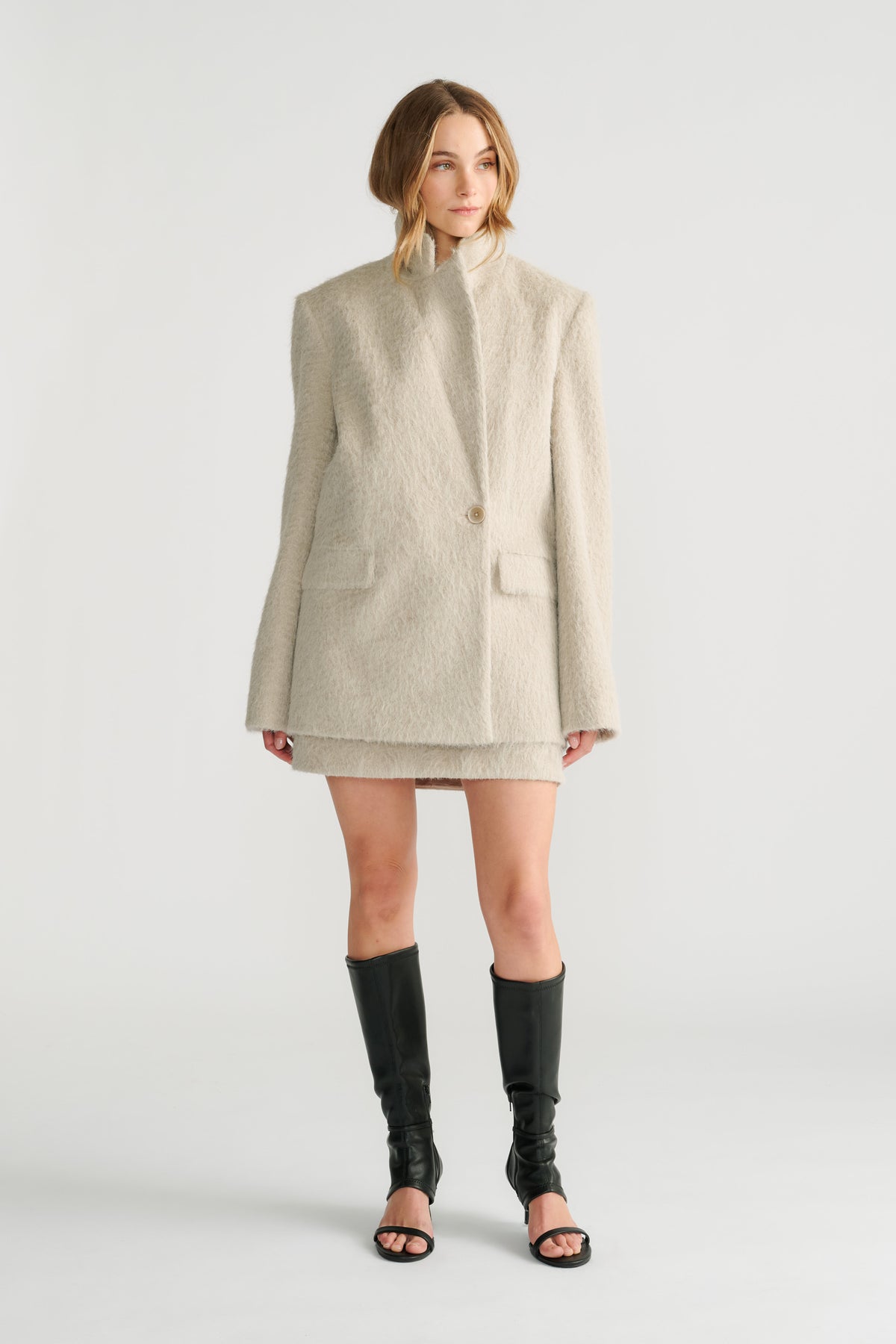 Model wearing a soft cream oversized blazer with long sleeves and notch lapels paired with black open-toe boots