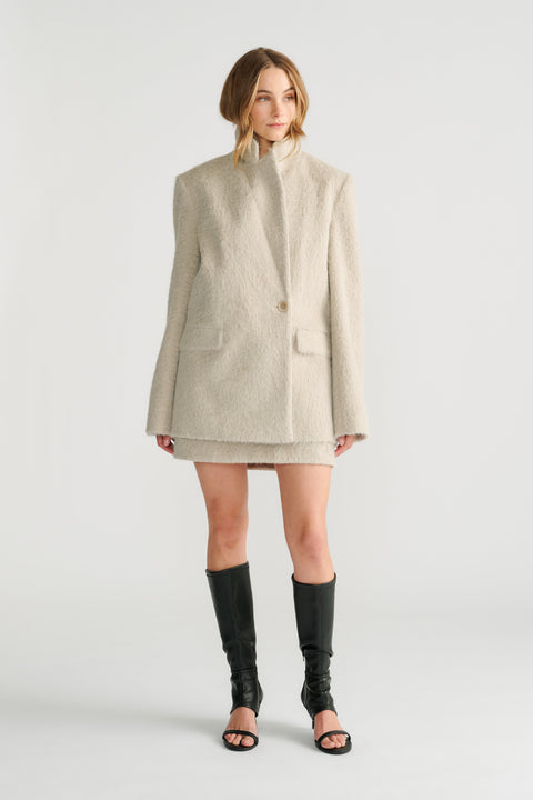 Model wearing a soft cream oversized blazer with long sleeves and notch lapels paired with black open-toe boots