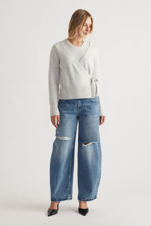 Woman wearing light grey Tamica Layered Jumper with wrap detail paired with relaxed blue ripped wide-leg denim jeans and black heels