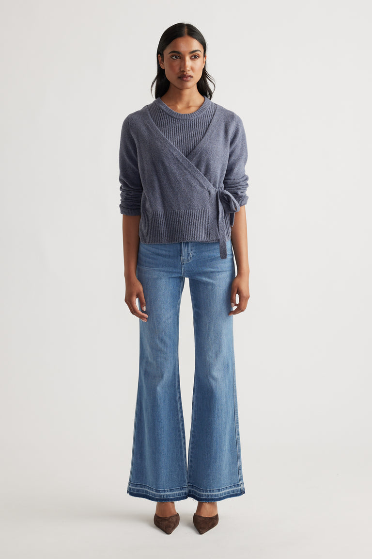 Woman wearing Tamica Layered Jumper in soft shadow blue layered over knit top, styled with flared denim jeans and pointed shoes