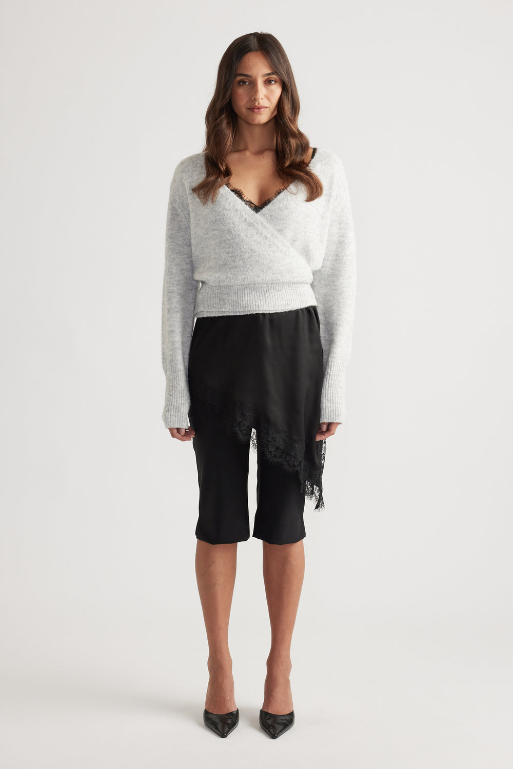 Soft light grey knit cardigan with a crossover front, ribbed waist and cuffs paired with a black lace-trimmed skirt
