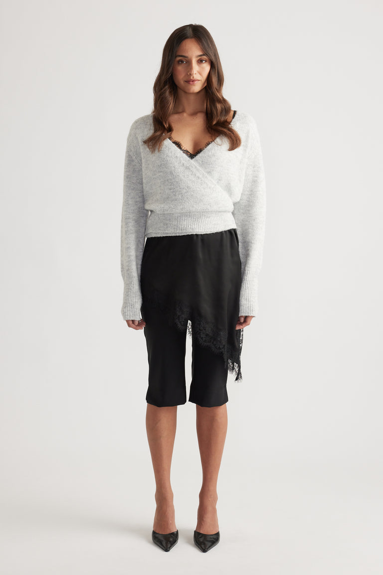 Soft light grey knit cardigan with a crossover front, ribbed waist and cuffs paired with a black lace-trimmed skirt