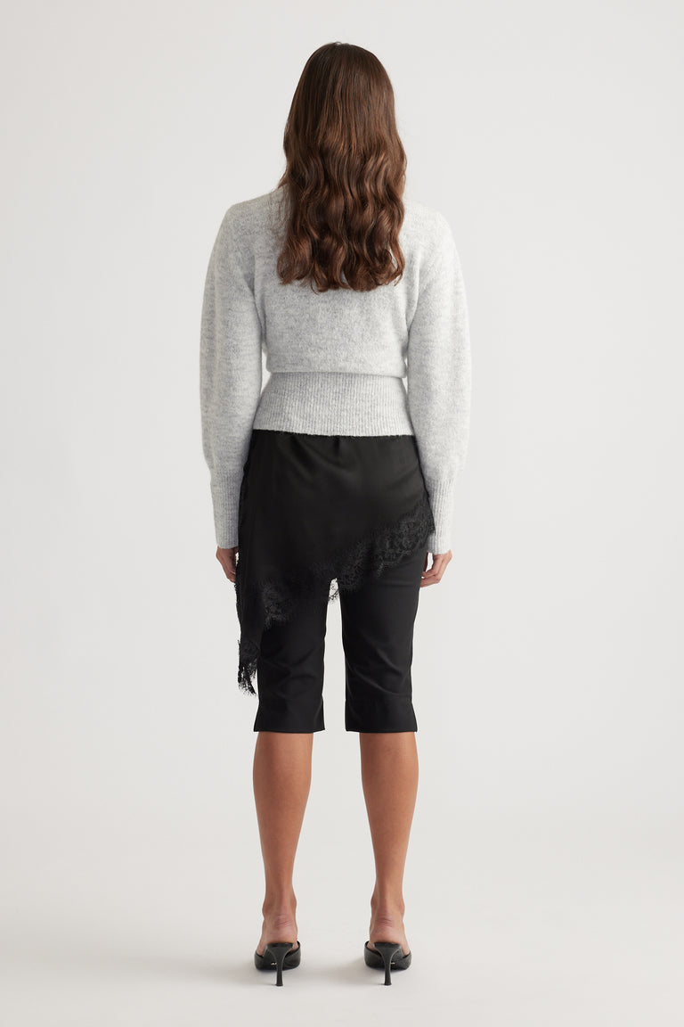 Back view of a soft grey knit crossover cardigan paired with a black asymmetrical lace-trimmed skirt and heels.