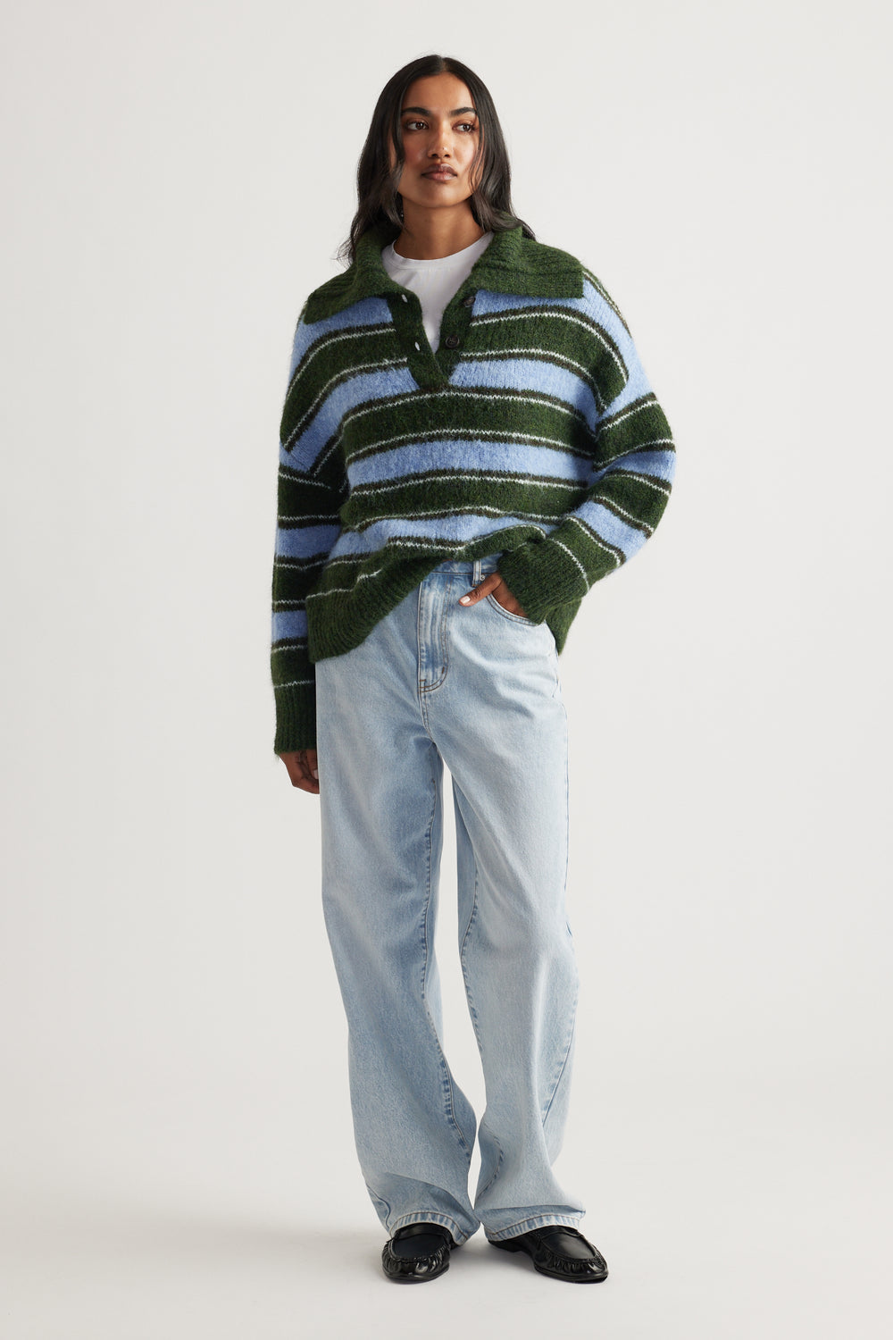 Woman wearing a cozy green and blue striped knit polo styled with light-wash relaxed fit jeans and black loafers.