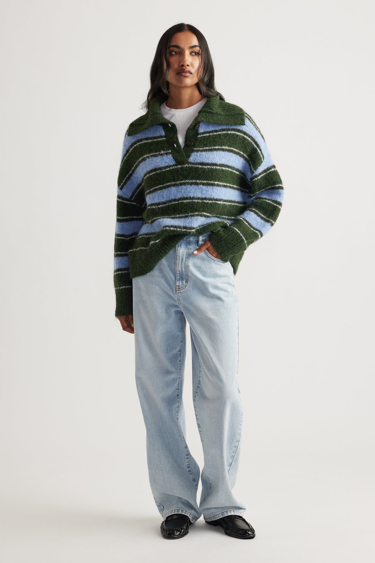 Woman wearing a cozy green and blue striped knit polo styled with light-wash relaxed fit jeans and black loafers.