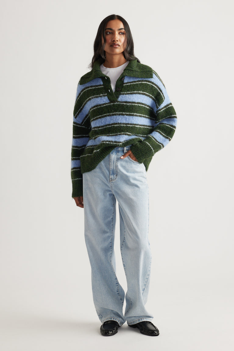 Woman wearing a cozy green and blue striped knit polo styled with light-wash relaxed fit jeans and black loafers.