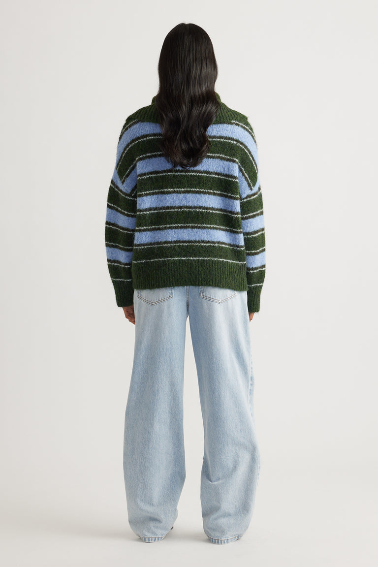 Back view of a woman wearing a striped knit jumper in green and blue paired with loose light-wash wide-leg jeans.