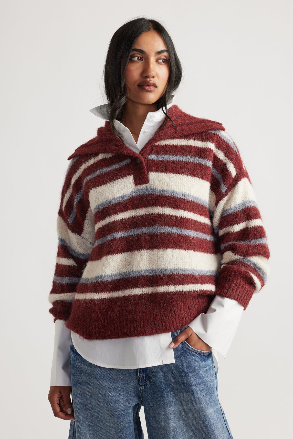Woman wearing Riley Knit Polo with red, cream, and blue stripes layered over white shirt and relaxed denim jeans by DECJUBA Australian brand
