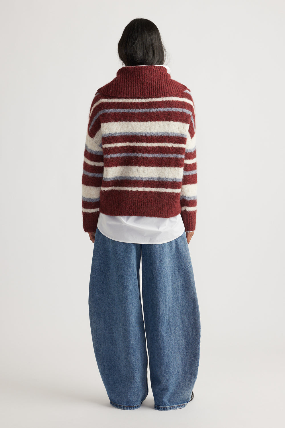 Back view of woman wearing Riley Knit Polo in maroon and cream stripes layered over white shirt with wide-leg denim jeans by DECJUBA Australian brand
