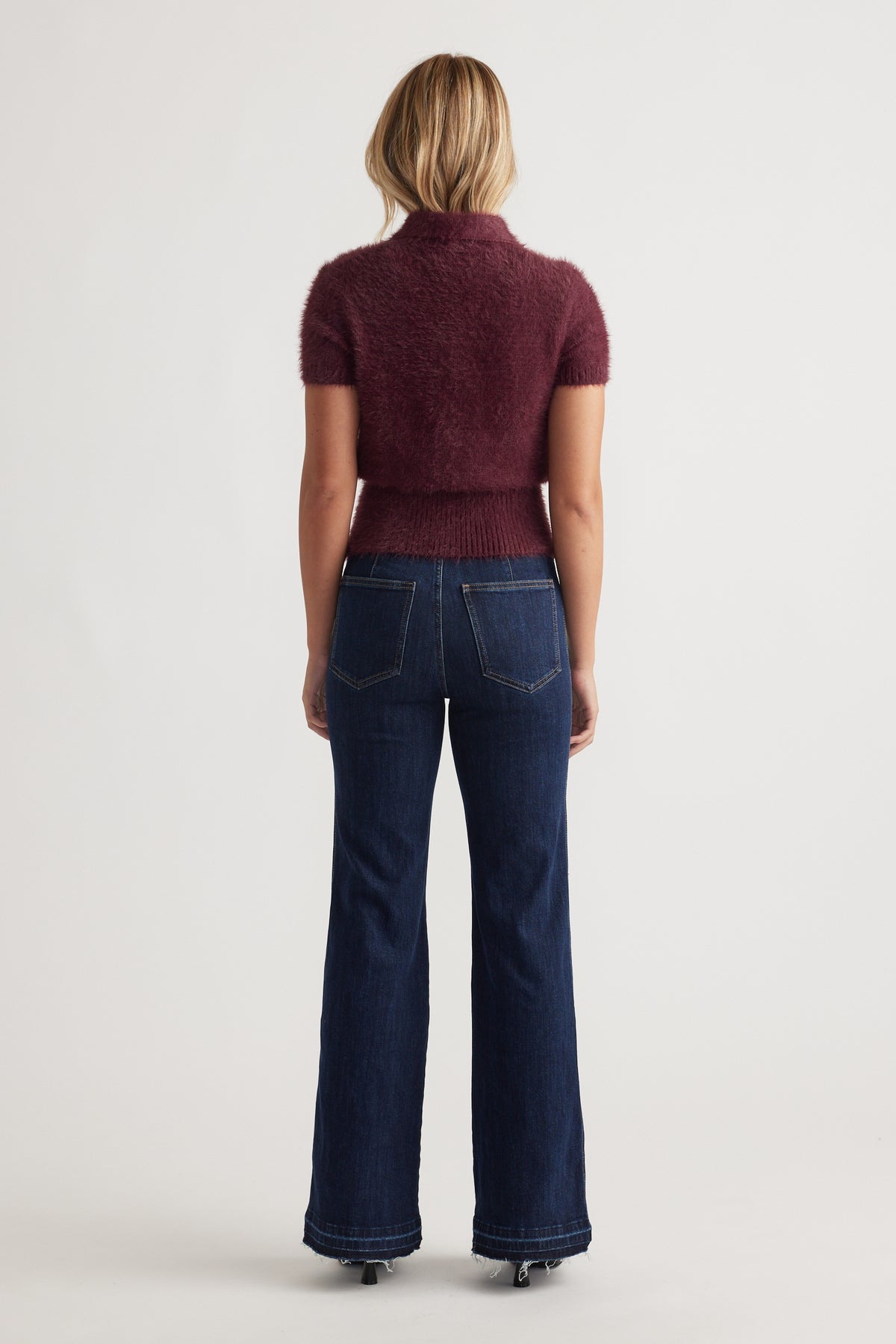 Back view of woman wearing plum Rosie Fluffy Knit Polo Tee with short sleeves paired with dark high-rise denim jeans