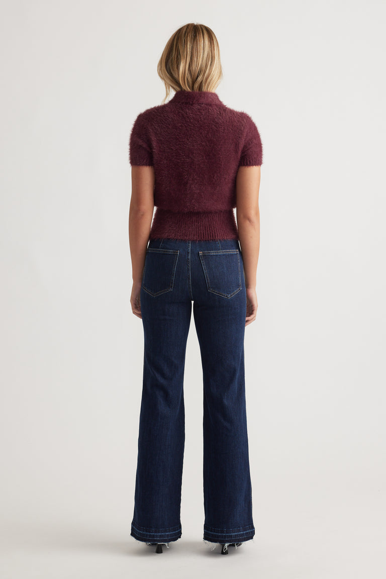 Back view of woman wearing plum Rosie Fluffy Knit Polo Tee with short sleeves paired with dark high-rise denim jeans