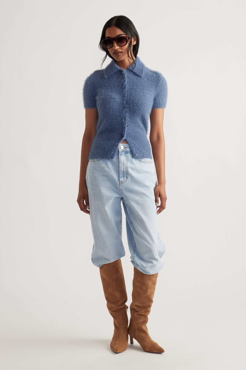 Woman wearing a steel blue Rosie Fluffy Knit Polo Tee with light wash jeans tucked into tan suede boots and sunglasses