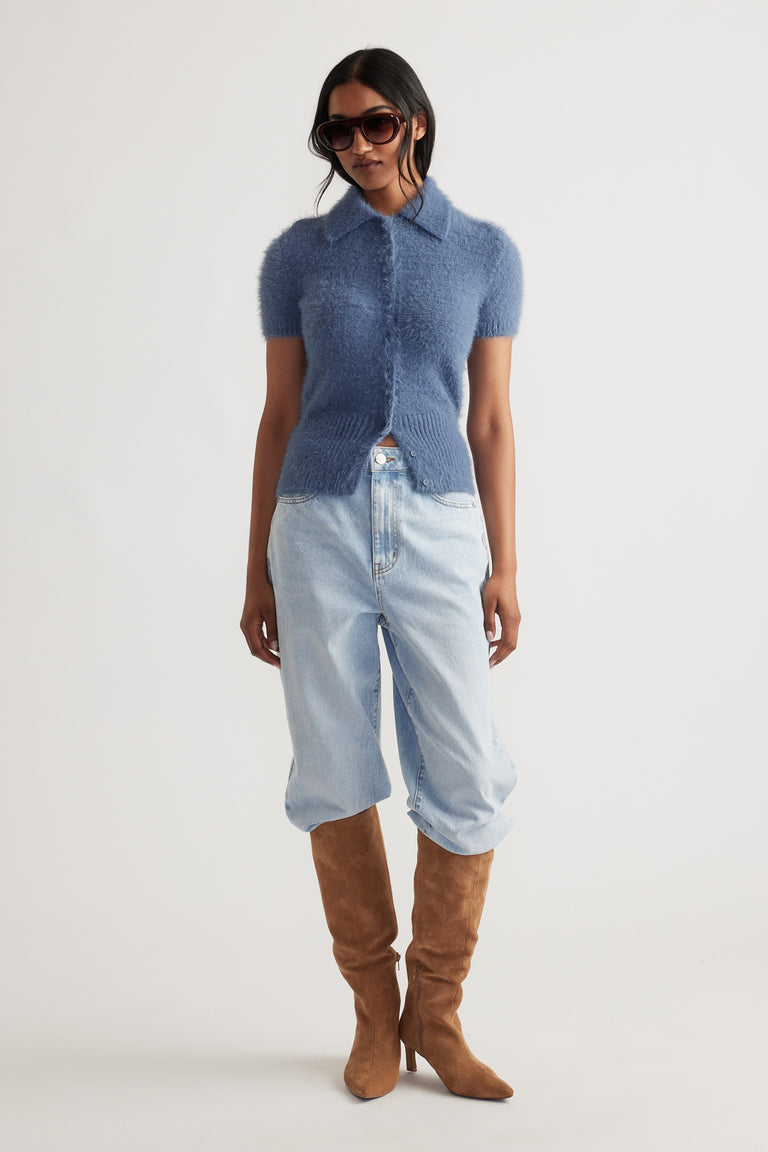 Woman wearing a steel blue Rosie Fluffy Knit Polo Tee with light wash jeans tucked into tan suede boots and sunglasses