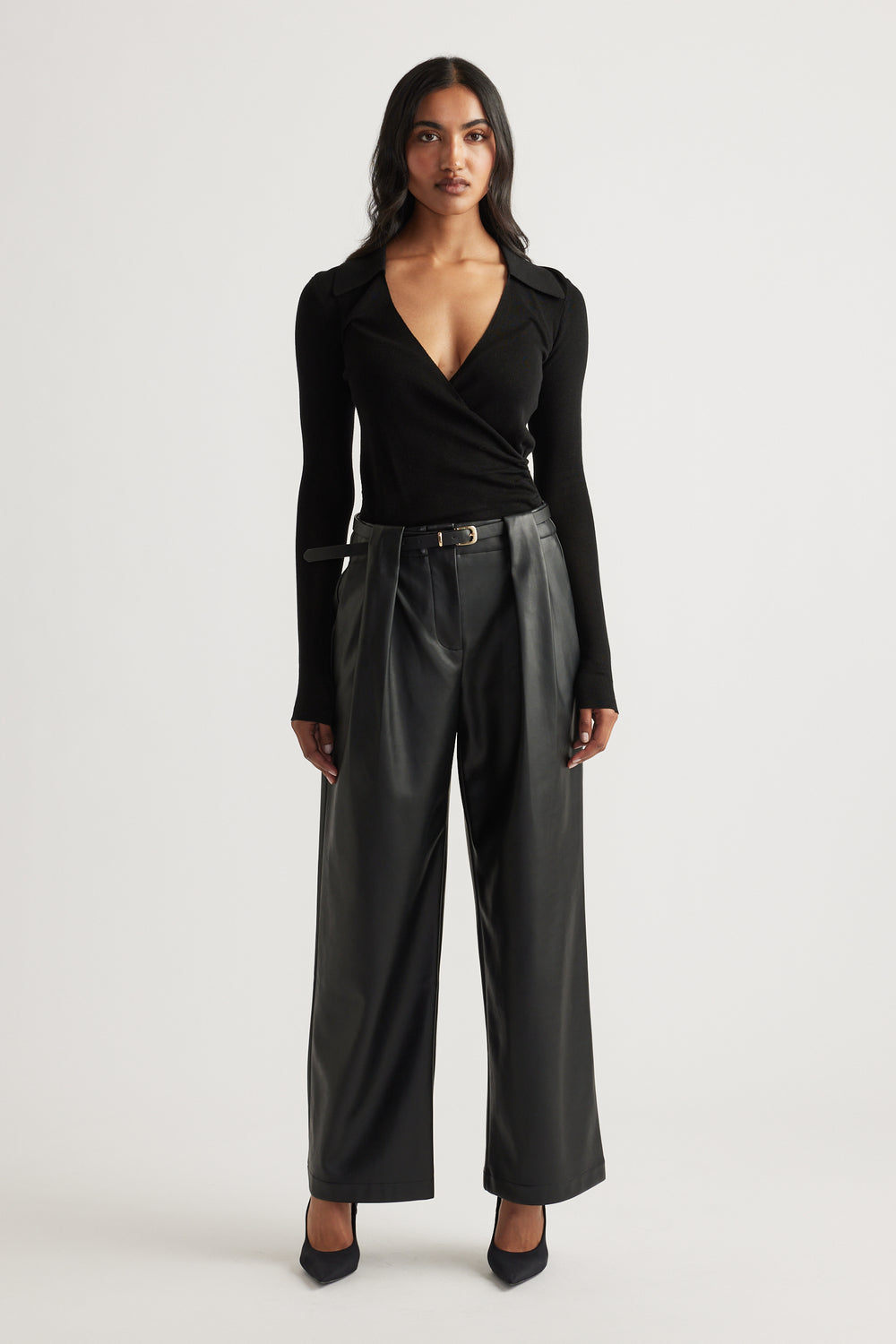 Woman wearing a fitted black crossover knit top paired with wide-leg faux leather trousers and pointed black heels