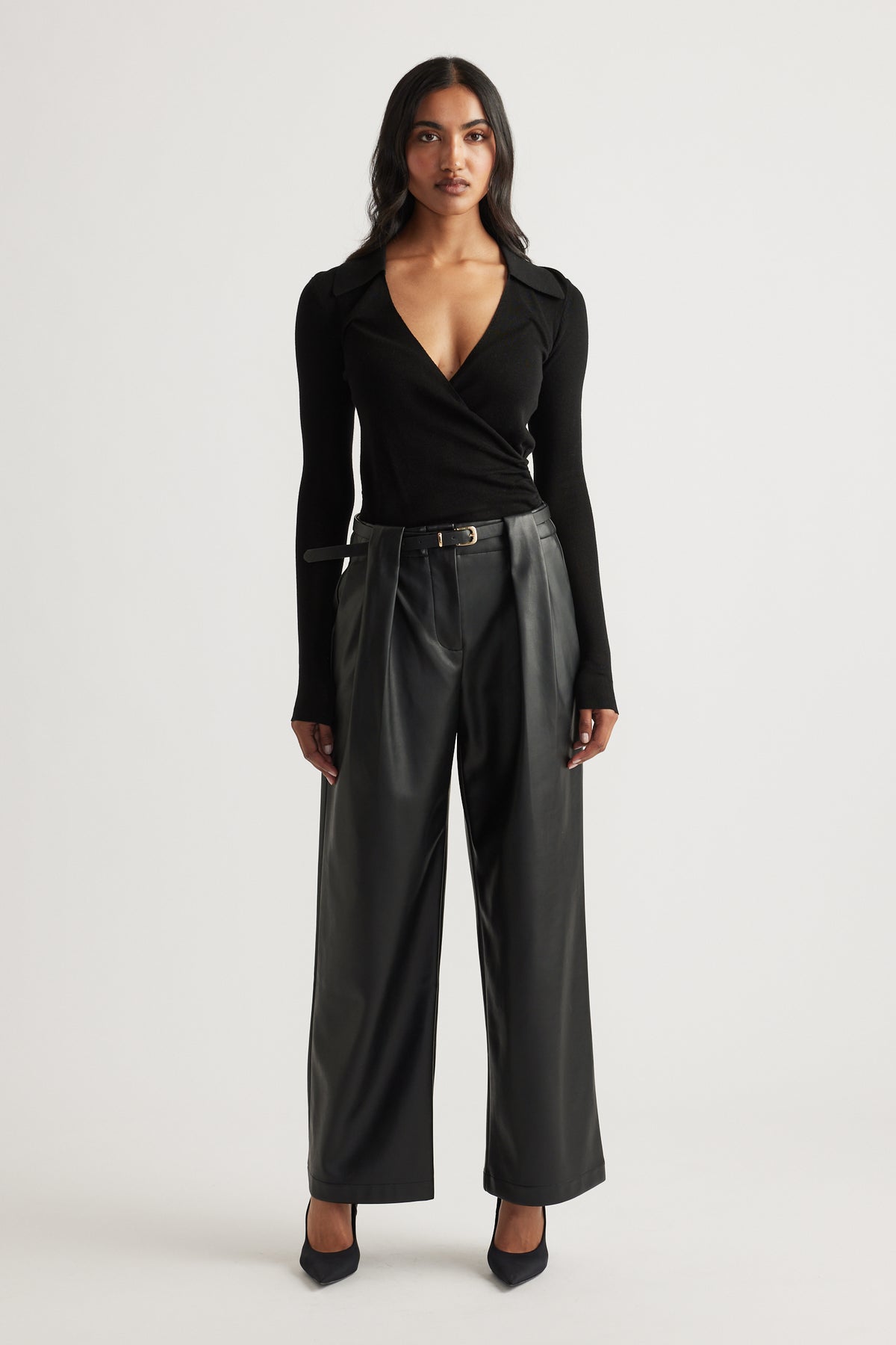 Woman wearing a fitted black crossover knit top paired with wide-leg faux leather trousers and pointed black heels