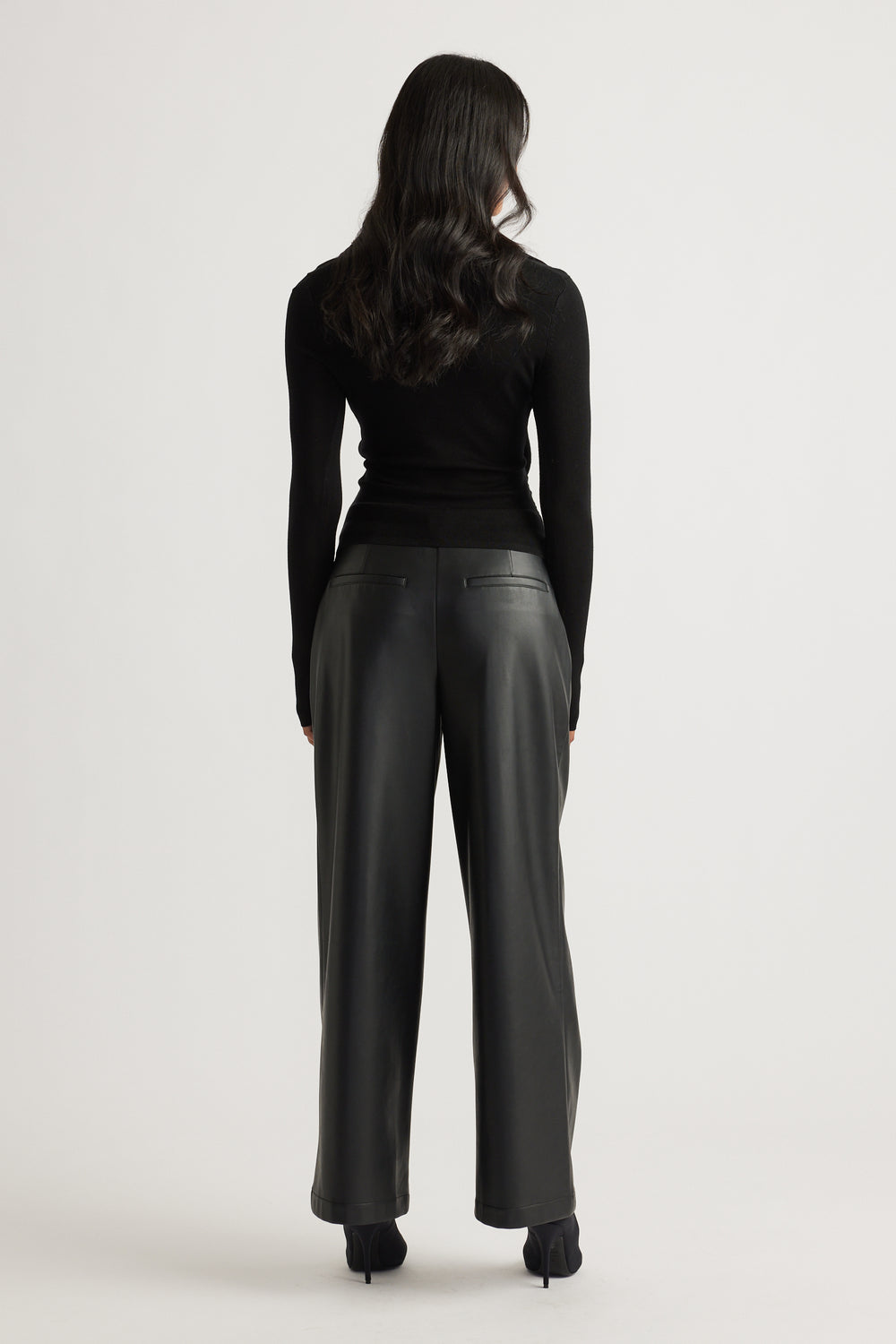 Woman wearing a fitted black knit top with long sleeves paired with high-waisted wide-leg black leather pants